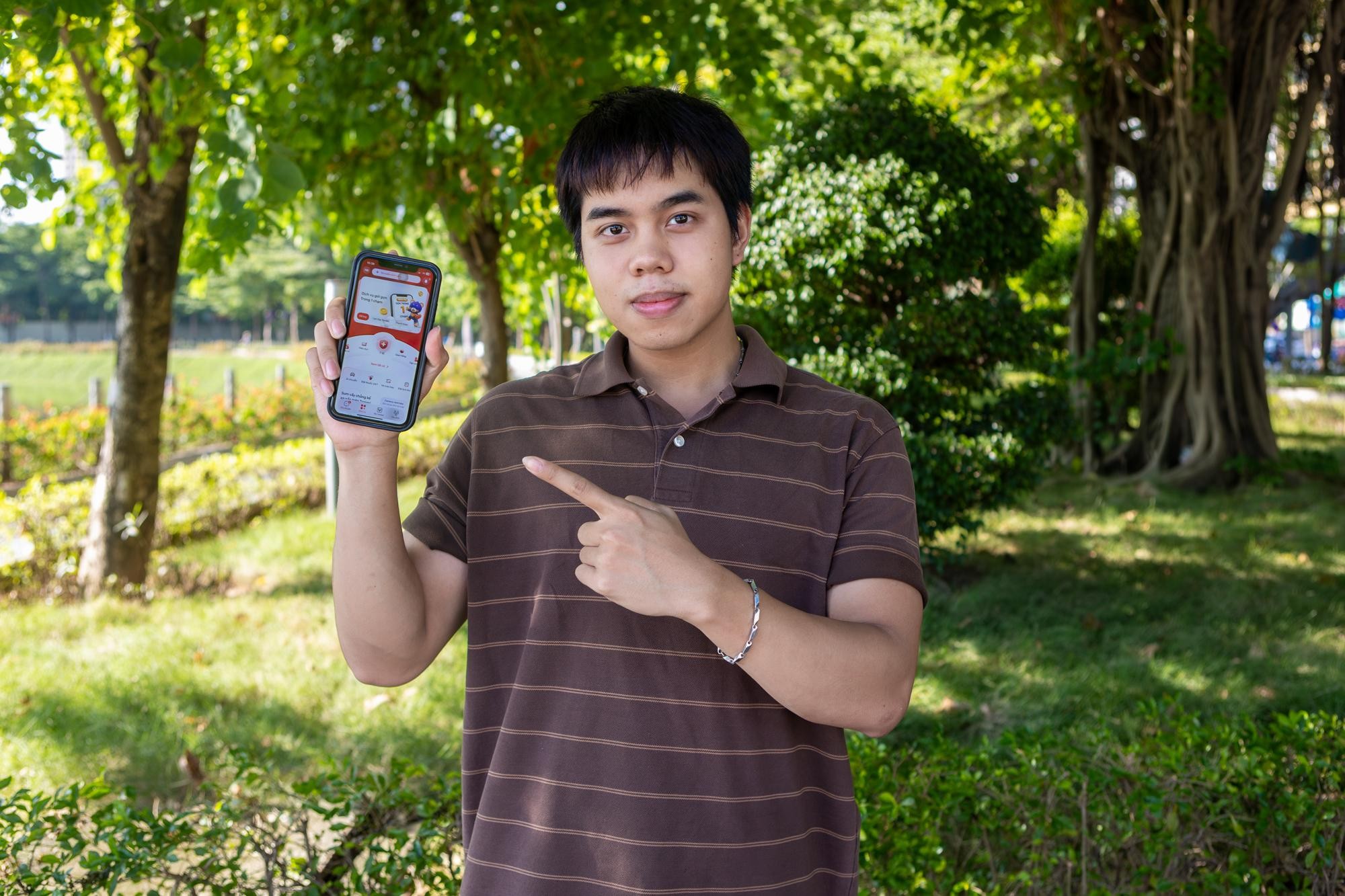 A young man outdoors holding a smartphone that displays the Viettel Tammi app