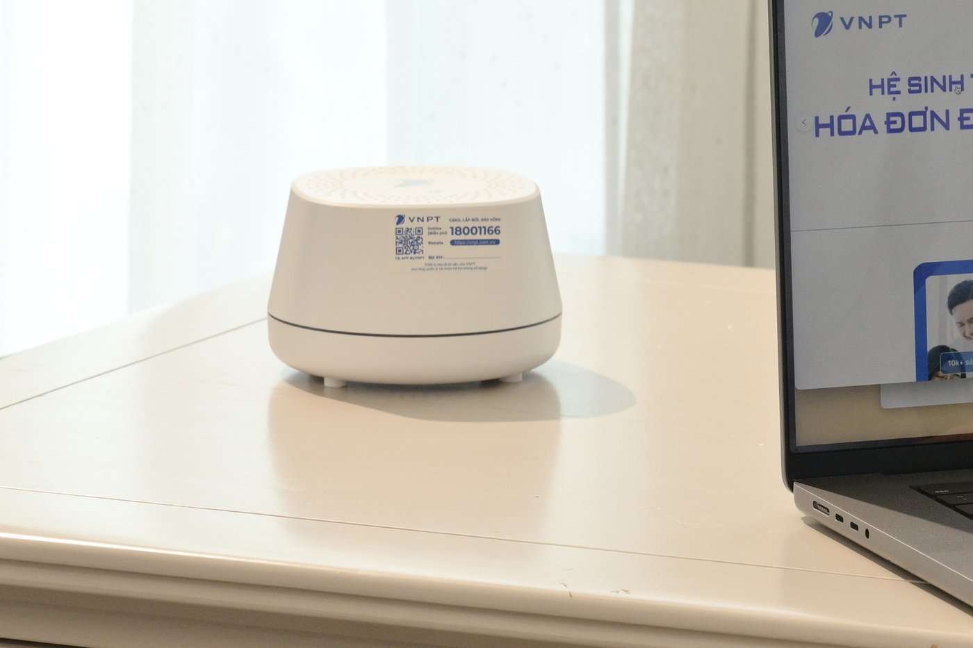 Close-up of a white VNPT network device with a hotline sticker on a desk, next to a laptop