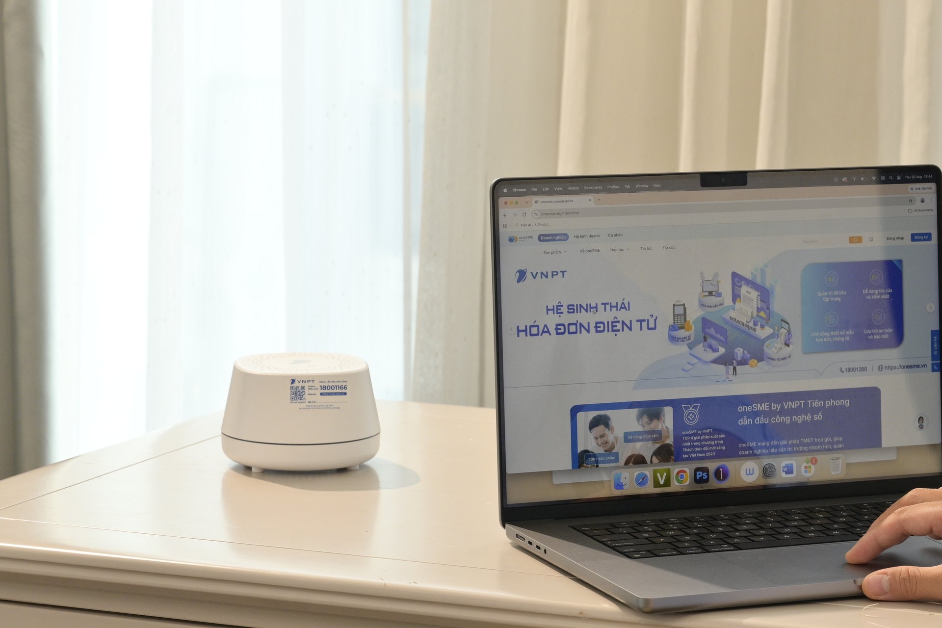 A desk with a white VNPT network device and a laptop showing the VNPT e-invoice ecosystem page, a hand resting on the trackpad